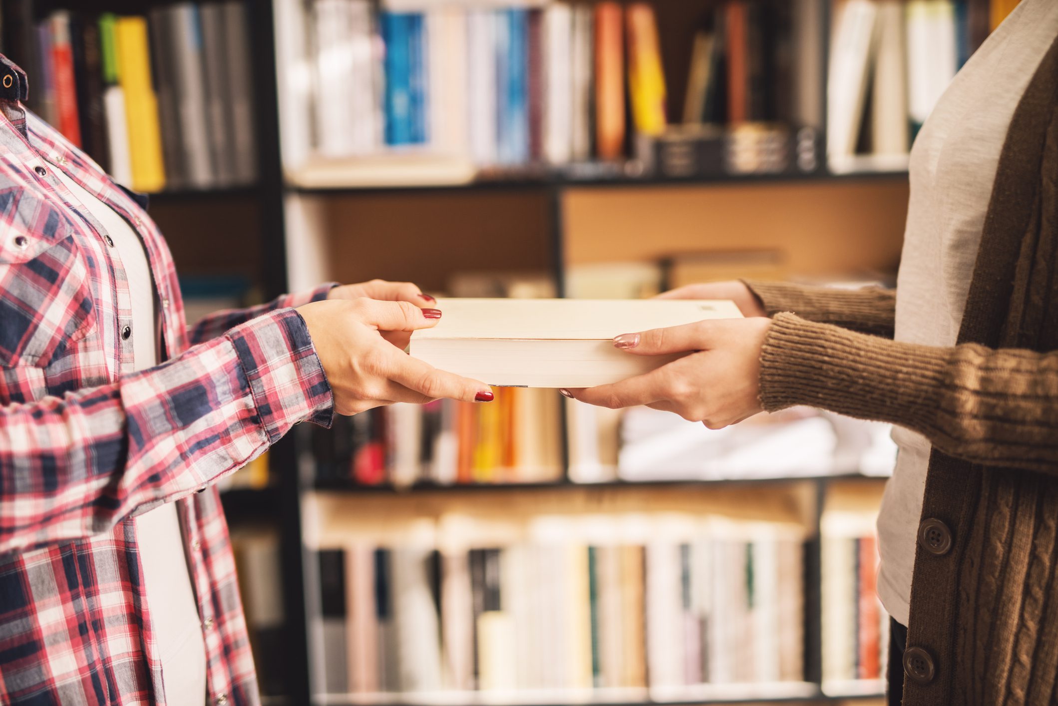 Two people exchanging a book in library.
